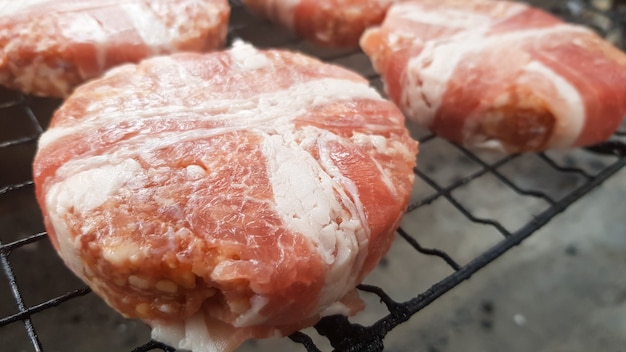 Auf dem Grillrost werden rohe Fleischkoteletts im Speckmantel gegart. Der Küchenchef bereitet die gegrillten Burger-Patties zu. Zutaten für die Herstellung eines Hamburgers. Konzept für Fleischliebhaber. Fastfood.