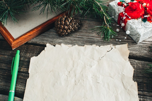 Auf dem Holztisch liegt ein altes gelbes Papier, auf dem steht: Lieber Weihnachtsmann rot, Bleistifte, Kugelschreiber verschiedene Farben Geschenk und Äste für das neue Jahr