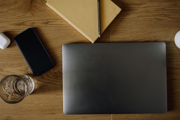 Foto auf dem holztisch stehen laptop, notebook, telefon und ein glas wasser. draufsicht des konzeptfotos