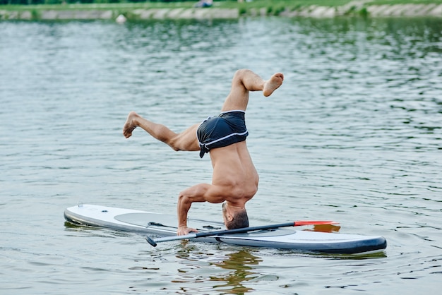 Foto auf dem kopf stehend, yogaübungen machend, schwimmend auf superboad im stadtsee.