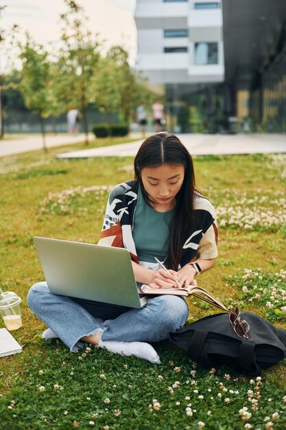 Auf dem Rasen mit Laptop auf den Beinen Junge asiatische Frau ist tagsüber im Freien