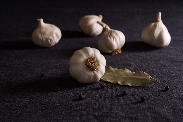 Auf dem schwarzen Tisch Gewürze: Zwiebel, Knoblauch, schwarze Pfeffererbsen und Lorbeerblatt