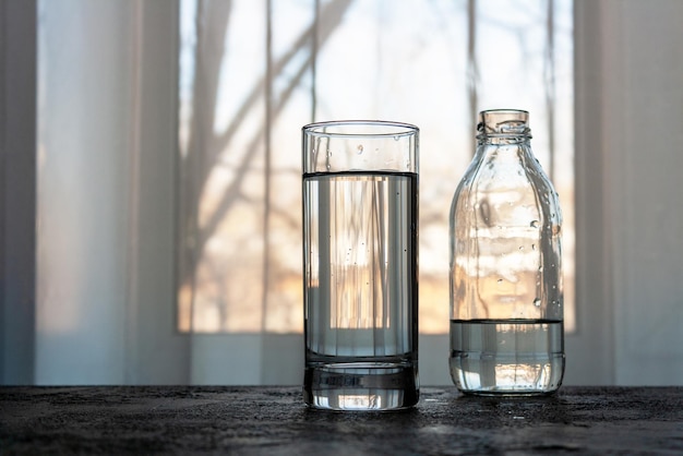 Auf dem Tisch am Fenster stehen ein Glas Wasser und eine Flasche