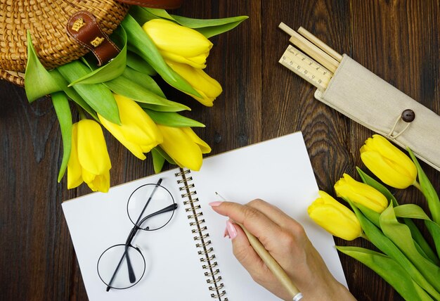 Auf dem Tisch befindet sich ein Notizbuch für Notizen und schöne gelbe Tulpen