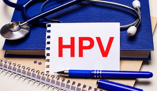 Auf dem Tisch liegen Notizblöcke, ein Stethoskop, ein Stift und ein Blatt Papier mit dem Text HPV Medical Concept