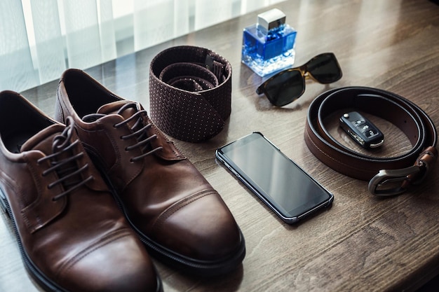 Auf dem Tisch liegen verschiedene Herrenaccessoires wie Schuhe, Gürtel, Krawatte, Brille, Autoschlüssel und Telefon