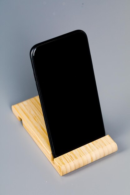 Auf dem Tisch liegt ein schwarzes Smartphone auf einem Holzständer. Ein Ort zum Kopieren.