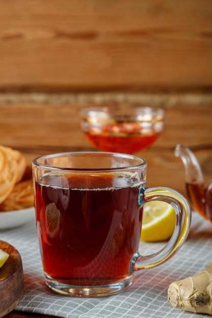 Auf dem Tisch steht eine Tasse starken Tee, im Hintergrund Zitrone und Ingwer, Donuts und Marmelade in einer Vase.