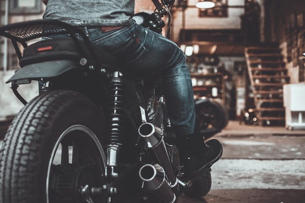 Foto auf dem weg zu seiner garage. nahaufnahme der rückansicht des mannes, der auf seinem fahrrad mit motorradgarage im hintergrund sitzt