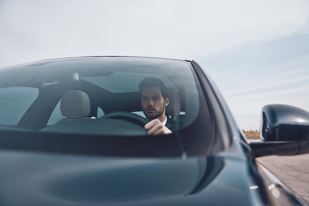 Auf dem Weg zum Geschäftstreffen. Hübscher junger Mann im vollen Anzug, der beim Autofahren gerade schaut