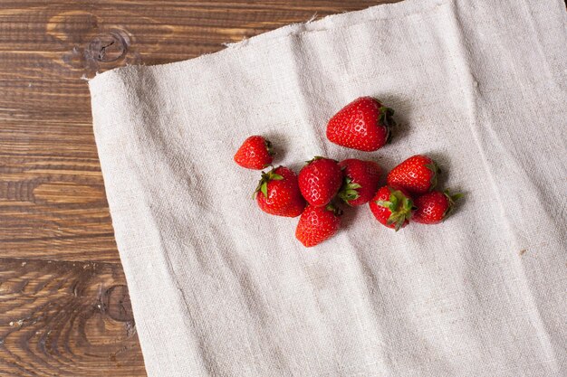 Auf dem weißen Küchentuch liegen frische rote Erdbeeren. Holzhintergrund