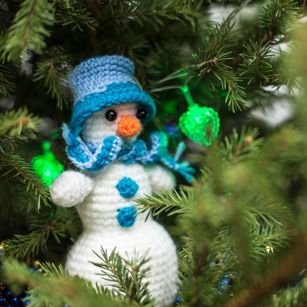 Auf den Zweigen eines Weihnachtsbaums sitzt ein süßer, selbst gestrickter Schneemann mit Hut und Schal