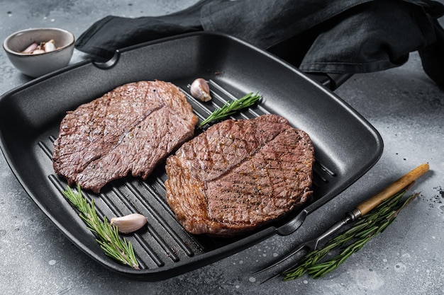 Auf der Grillpfanne gebratene marmorierte Fleischsteaks vom Rind. Grauer Hintergrund. Ansicht von oben.