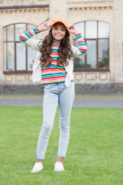 Auf der Suche nach einem trendigen Konzept eines gesunden Lebensstils, süßes kleines Mädchen hat lockiges Haar, brünettes Kind in Straßenfrühlingsmode und Schönheit