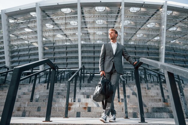 Auf der Treppe des Stadions Junger Geschäftsmann in grauer Abendgarderobe ist draußen in der Stadt