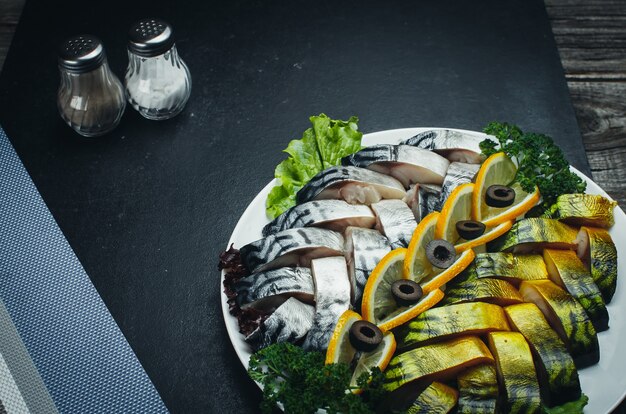 Auf dunklen Stoffen ist auf dem Teller ein wunderschöner Fisch, Hering und Lachs mit Grün verziert