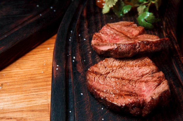 Auf einem alten Holzbrett werden dicke saftige Portionen gebratenes Filetsteak serviert, mit Salz bestreut. Das Gericht ist servierfertig.