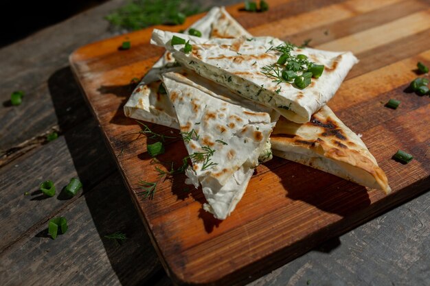 Auf einem Brett liegt ein Gericht aus Hüttenkäse mit Petersilie und Zwiebeln in Fladenbrot, das auf einem Rost gebraten wird