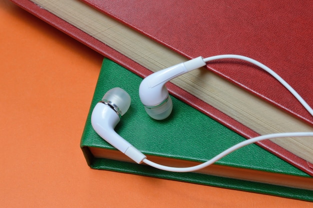 Auf einem Bücherstapel liegen kleine weiße Kopfhörer mit Kabel. Nahansicht