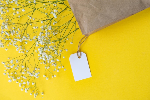 Auf einem bunten gelben Tisch liegt ein Modell eines Etiketts und eines Preisschilds in der Nähe einer Basteltasche mit Blumen