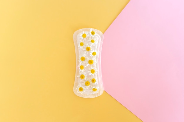 Auf einem bunten Hintergrund liegt eine Damenbinde mit Kamillenblüten. Menstruationstage. Hygiene- und Frischekonzept