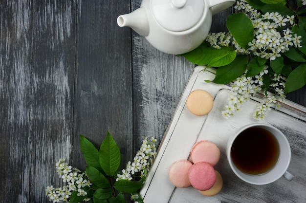 Auf einem grauen Hintergrund gibt es ein Tablett, eine weiße Teekanne, eine Tasse Tee und Kirschblüten