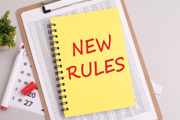 Foto auf einem grauen hintergrund liegt ein weißes dokument, ein roter marker, wäscheklammern und ein gelbes notizbuch mit der inschrift new rules