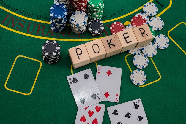 Auf einem grünen Pokertisch liegen Karten, Chips und die Aufschrift Poker auf Holzwürfeln. Pokerkonzept