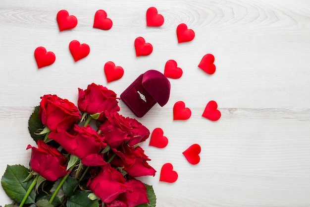 auf einem hellen Holztisch rote Rosen, Dekor in Form von Herzen und Verlobungsring