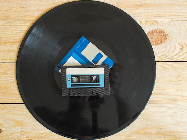 Foto auf einem hölzernen hintergrund befindet sich eine vinylplatte und darauf eine audiokassette und eine diskette