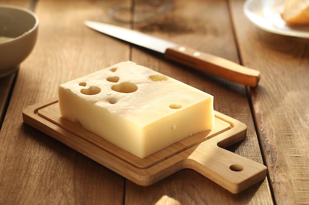 Auf einem Holzbrett auf dem Tisch liegt ein Stück Käse. Daneben liegt ein Messer. Der Raum ist von Sonnenlicht durchflutet