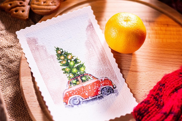 Auf einem Holzbrett liegt eine Neujahrskarte mit Schreibmaschine und Weihnachtsbaum, daneben eine Mandarine. Lebkuchen im Hintergrund