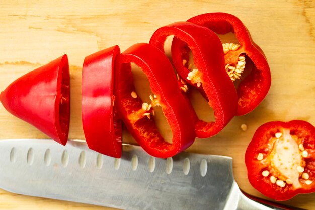 Auf einem Holzbrett neben einem Messer liegt eine in Ringe geschnittene rote Paprika. Konzept einer gesunden Ernährung