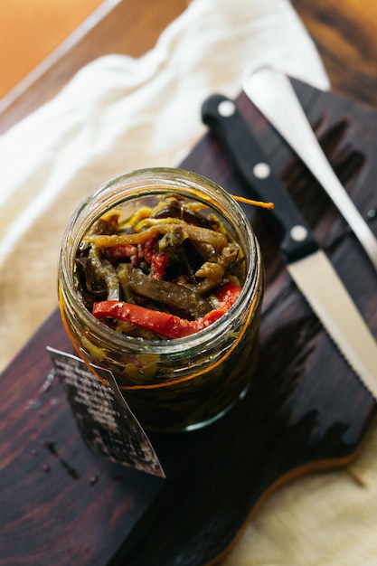 Foto auf einem holzbrett steht ein glas eingelegter paprika, daneben ein messer.