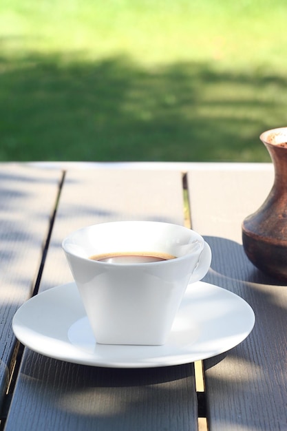 Auf einem Holztisch im Garten steht eine Tasse Kaffee. Dahinter steht ein Türke mit frisch gebrühtem Kaffee