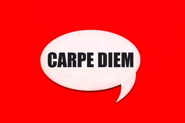 Auf einem leuchtend roten Hintergrund eine helle gelockte Holzkarte mit dem Text CARPE DIEM