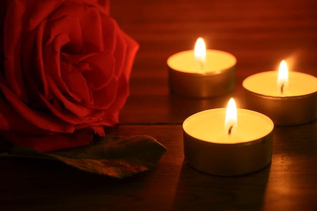 Auf einem Tisch liegt eine rote Rose und drei Kerzen brennen