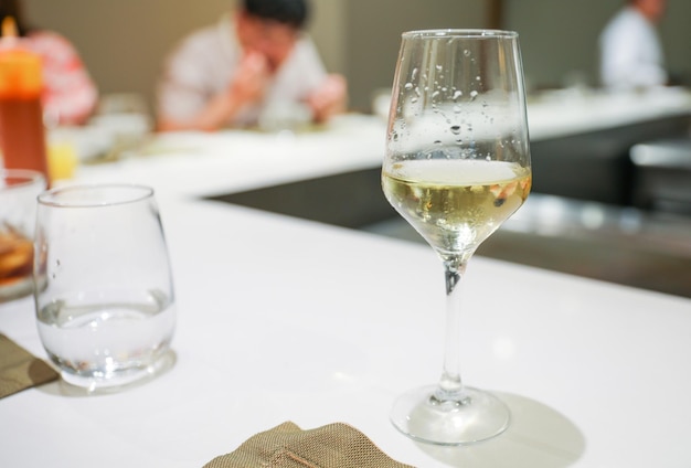 Auf einem Tisch steht ein Glas Wein, im Hintergrund ein Mann.