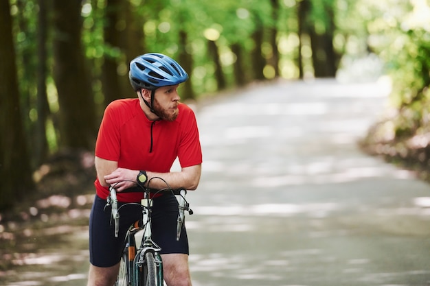 Auf einen Freund warten. Radfahrer auf einem Fahrrad ist auf der Asphaltstraße im Wald am sonnigen Tag