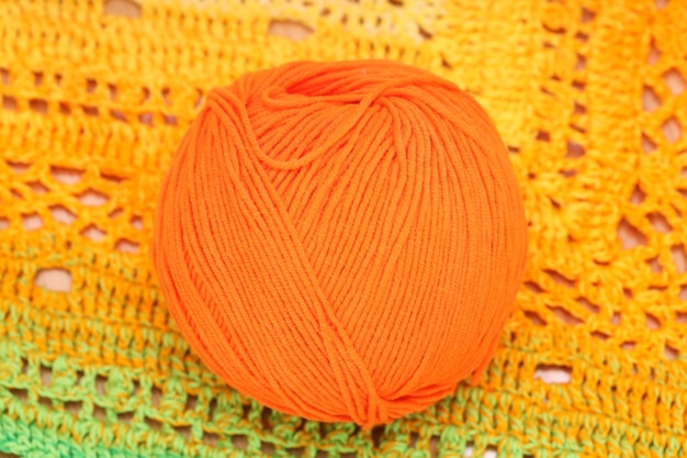 Auf einer gestrickten Serviette liegt ein orangefarbener Wollknäuel. Foto in hoher Qualität