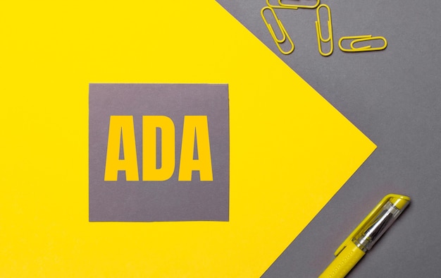 Auf grau-gelbem Hintergrund ein grauer Aufkleber mit gelbem Text ADA Americans with Disabilities Act, gelben Büroklammern und einem gelben Stift