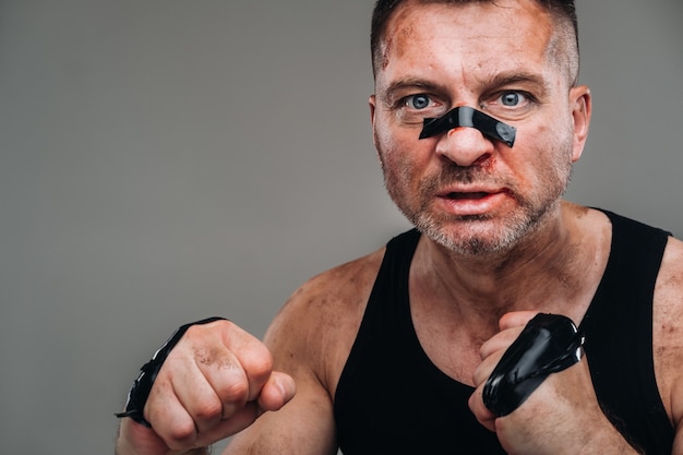 Auf grauem Hintergrund steht ein angeschlagener Mann in einem schwarzen T-Shirt, der wie ein Kämpfer aussieht und sich auf einen Kampf vorbereitet.