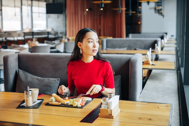 Auf grauem Sofa Dunkelhaarige Frau sitzt auf grauem Sofa im Restaurant und genießt ihr Mittagessen