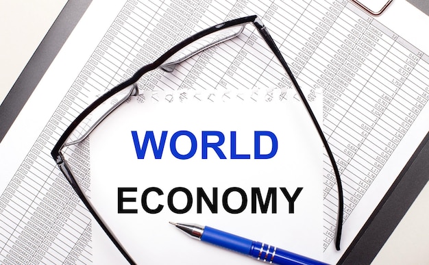 Auf hellem Hintergrund ein Bericht mit schwarzgerahmter Brille, einem Stift und einem Blatt Papier mit dem Text WORLD ECONOMY Business Concept