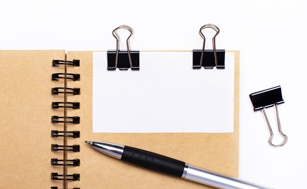 Auf hellem Hintergrund ein braunes Notizbuch mit Stift, schwarzen Clips und einer weißen Karte mit Platz zum Einfügen von Text oder Illustrationen. Schablone.
