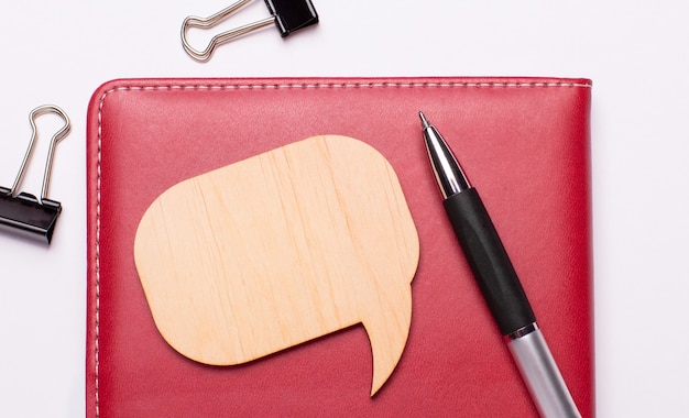 Auf hellem Hintergrund - schwarze Büroklammern, ein Stift, ein weinrotes Notizbuch und eine Holztafel mit Platz zum Einfügen von Text. Schablone.