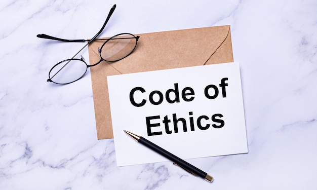 Auf hellem Marmorhintergrund ein Handwerksumschlag, eine Stiftbrille und ein Blatt Papier mit dem Text CODE OF ETHICS Business Concept