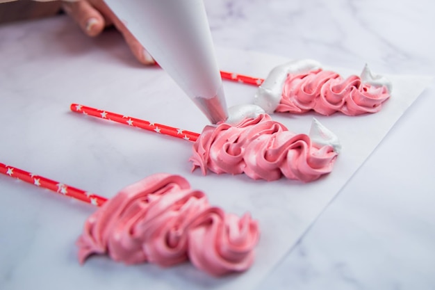 Auf hellem Pergament gibt es rosa Baiserkappen, auf Stäbchen macht der Koch einen Bommel und eine Rüsche aus einem