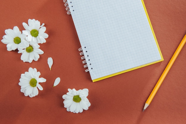 Auf hölzernem Notizbuchbleistift Kaffee und Blumen.