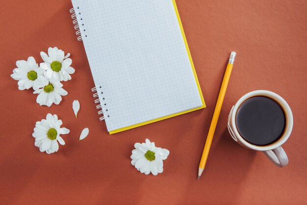 Auf hölzernem Notizbuchbleistift Kaffee und Blumen.